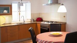 Eine kleine Küche mit einem Gasherd, einem roten Toaster und einem Spülbecken. Ein Tisch mit einer gestreiften Tischdecke und einer Schüssel darauf.