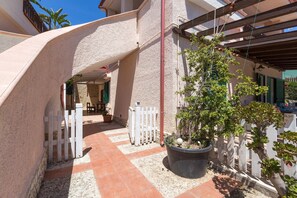 A courtyard with a white picket fence, a potted plant, and a tiled floor.