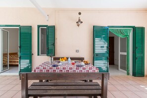 A dining area with a table set for two, a bench, and a view of a bedroom through an open door.