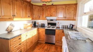 Una cocina con armarios de madera, estufa, lavaplatos y ventana.