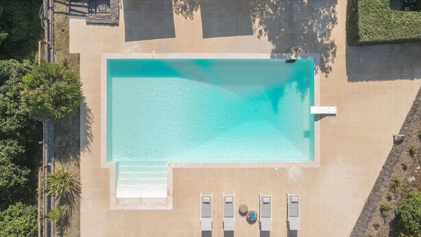 An aerial view of a rectangular swimming pool with a tiled deck surrounding it. There are lounge chairs and a small round table with a drink. - Villa Chimia 8 (Acireale)