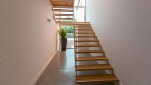 A modern staircase with wooden steps and a glass railing, leading to a bright area with a view of greenery outside. - Villa Chimia 8 (Acireale)