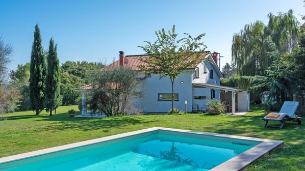 A house with a swimming pool, surrounded by greenery and trees.