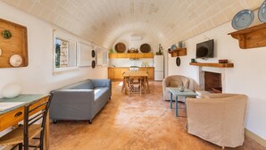 A cozy living room with a fireplace, a dining area, and a kitchen in the background. - 2770 Uliveto Valeria - Trullo Melograno by Perle di Puglia (San Michele Salentino)