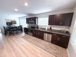 A modern kitchen with dark cabinetry, stainless steel appliances, and a dining area with a wooden table and chairs.