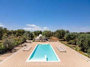 Piscina retangular com centro azul cristalino, rodeada por um deck ladrilhado com espreguiçadeiras.