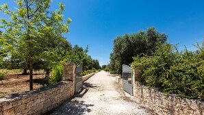 A gravel path flanked by stone walls and trees, leading to a gated entrance. - 1963 Villa Ajeni by Perle di Puglia (San Michele Salentino)