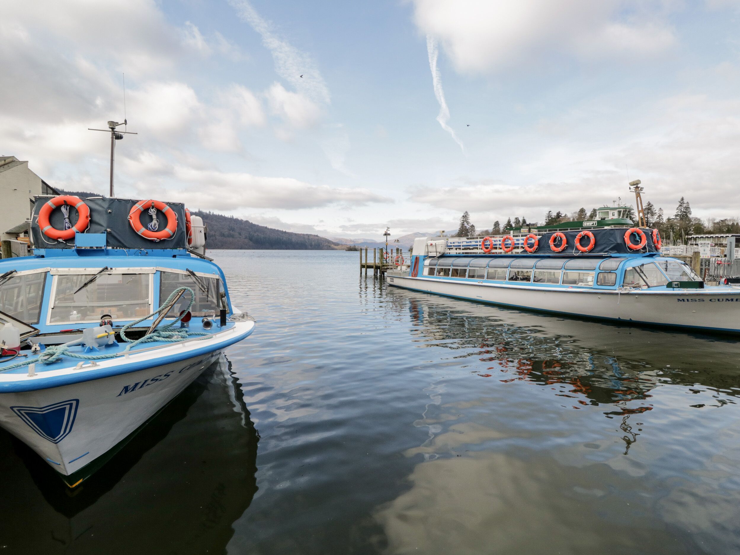 Two boats docked at a marina with lifebuoys on the side of the boats.