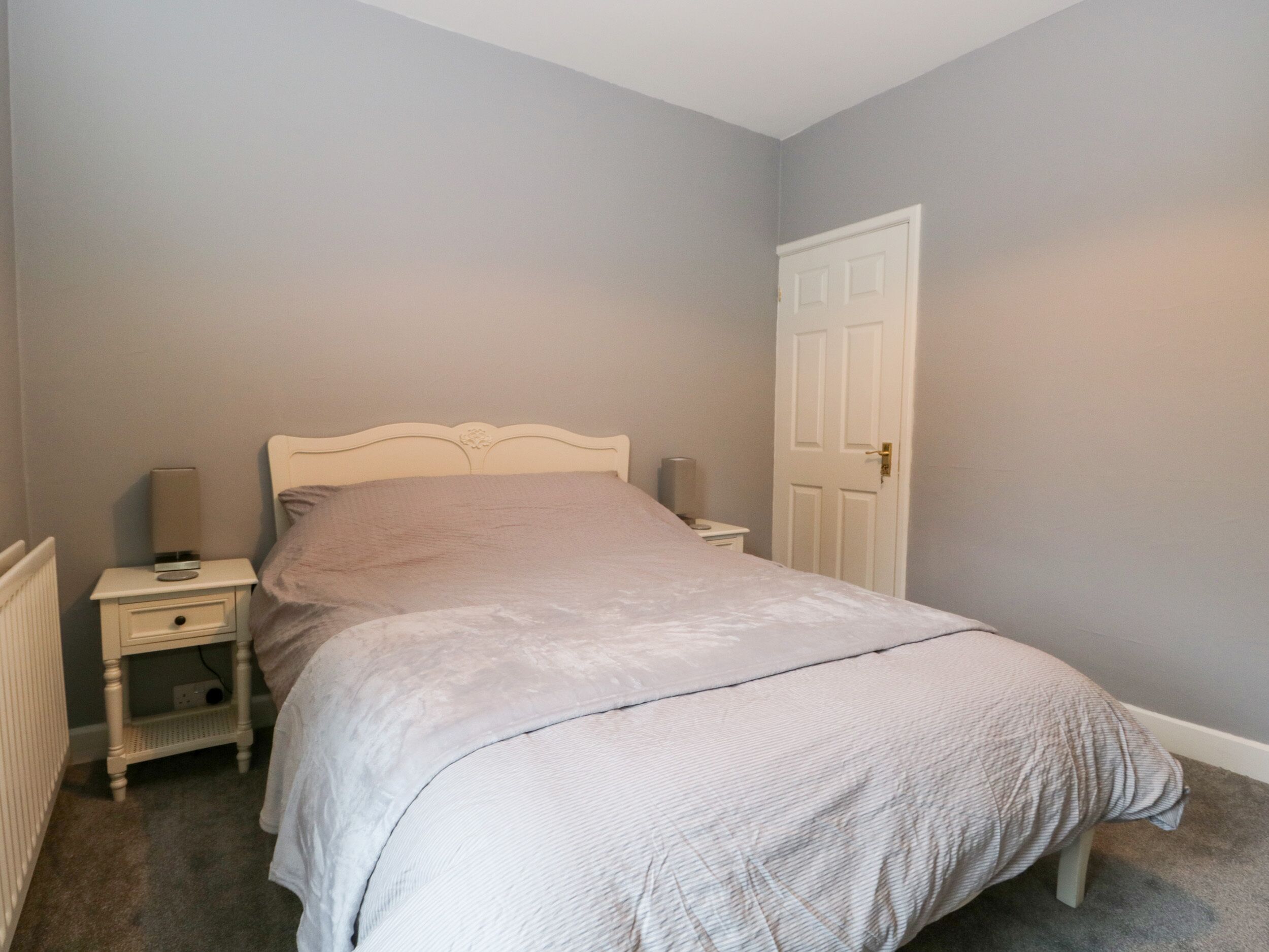 Une chambre avec un lit simple, une table de chevet, une lampe et une porte.