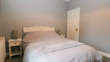 Une chambre avec un lit simple, une table de chevet, une lampe et une porte.