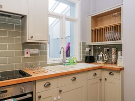 A kitchen with a window, a sink, a stove, and a shelf with dishes.
