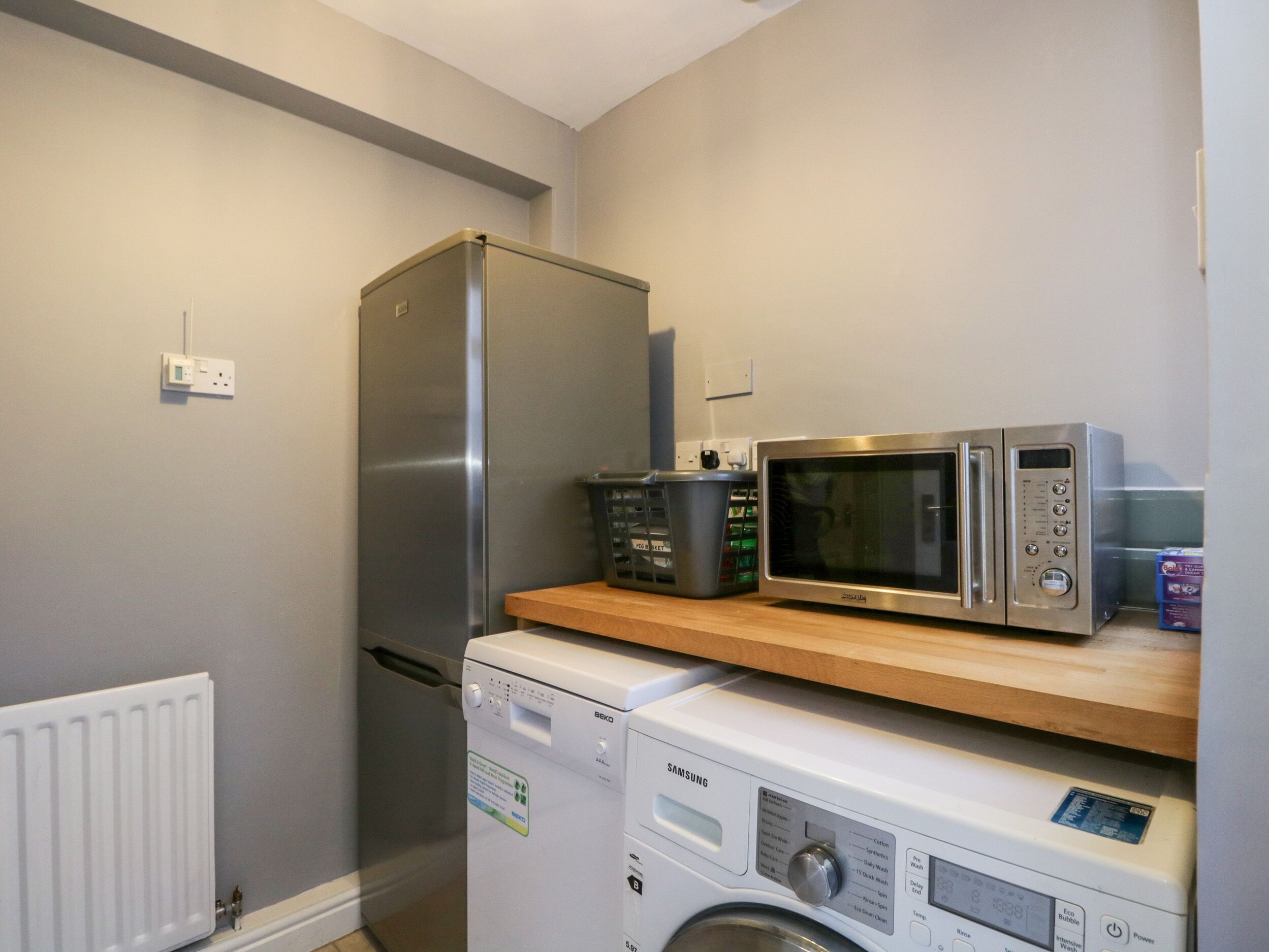 A compact kitchen with a stainless steel refrigerator, a microwave, and a washing machine.