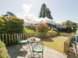 A garden patio with a table and chairs, a wooden fence, and a steam train in the background.