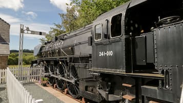Una locomotora de vapor negra, número 241-010, estacionada en una estación con una cerca blanca y follaje al fondo.
