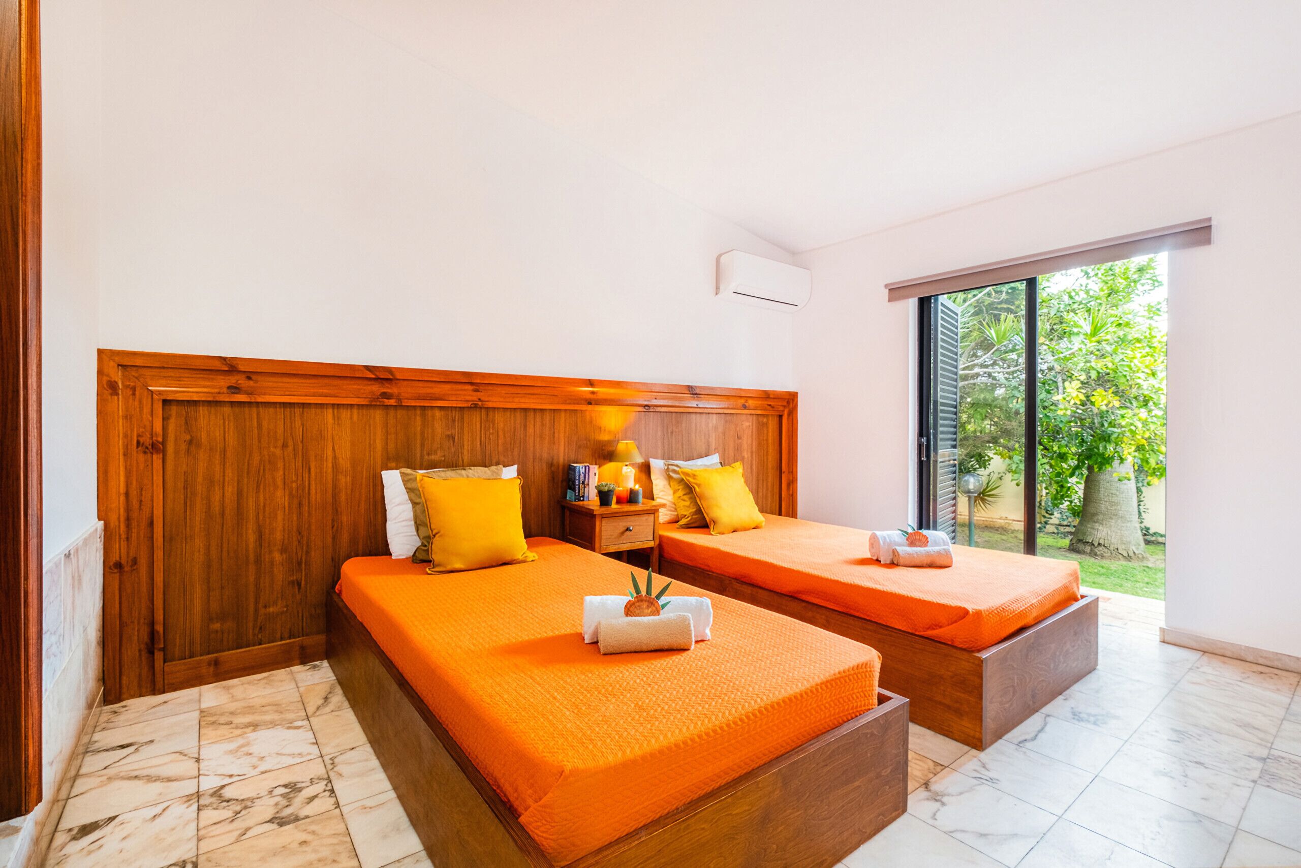 A room with two beds, wooden headboards, and a large window.