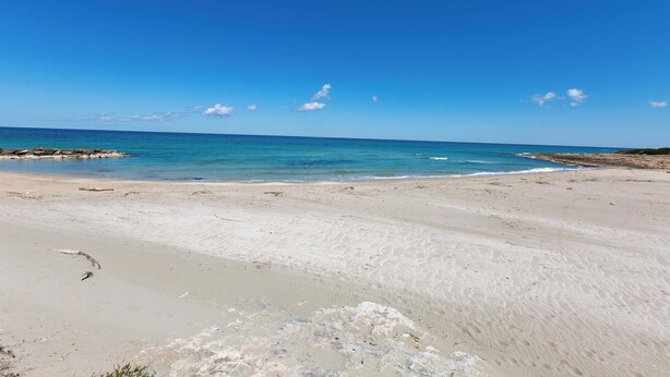 A beach with clear blue water and a sandy shore.
