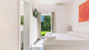 A bedroom with a bed, a TV mounted on the wall, a window with curtains, and a view of greenery outside.