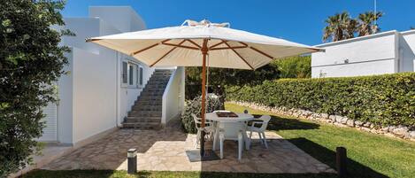 A patio with a table and chairs, a large umbrella, and a staircase leading to an upper level.