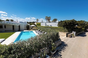 A swimming pool with lounge chairs, a stone wall, and a clear blue sky. - 2324 Villa Milhouse by Perle di Puglia (Ostuni)