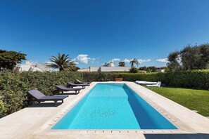 A rectangular swimming pool with lounge chairs and a wooden bench along its edge. - 2324 Villa Milhouse by Perle di Puglia (Ostuni)