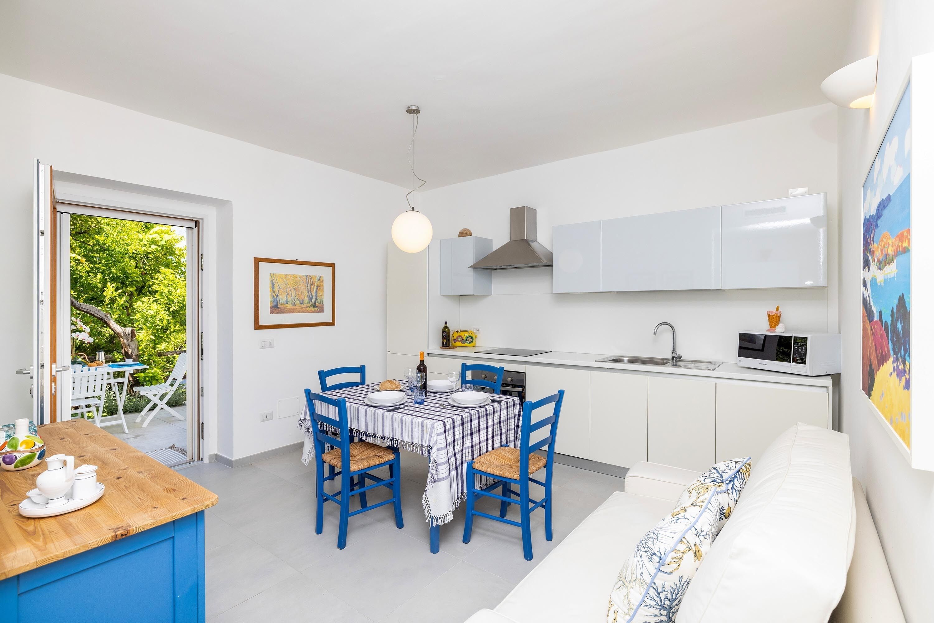 A compact kitchen with white cabinets, a dining table with blue chairs, and a white sofa.