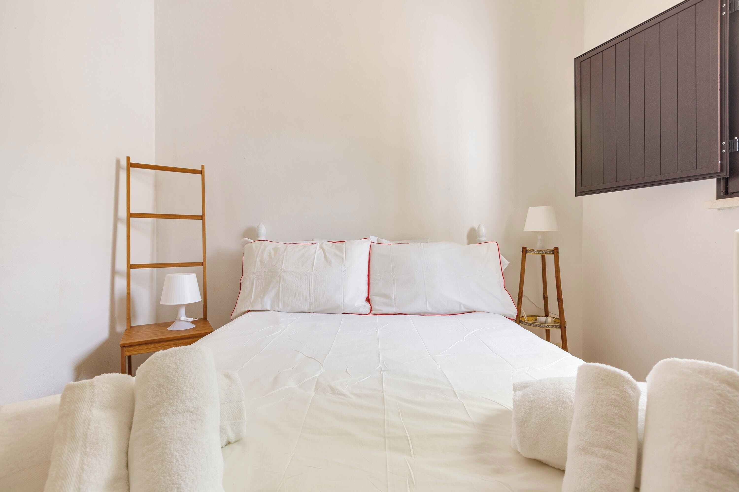 A bedroom with a bed, a nightstand with a lamp, a wall-mounted cabinet, and a ladder.