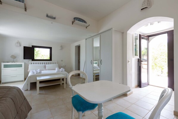 Une chambre à coucher comprenant un lit, une table de chevet, une armoire, ainsi qu’un coin repas avec une table et des chaises.