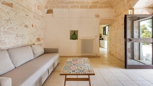 Ein Zimmer mit Steinwand, einer Couch, einem Tisch mit Muster und Blick durch eine Glastür.