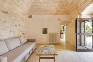 Quarto com parede de pedra, um sofá, uma mesa estampada e vista através de uma porta de vidro.
