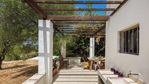 Ein überdachter Außenbereich mit einer Pergola, einem Esstisch mit Stühlen und Blick auf die umliegende Landschaft.