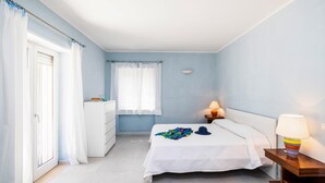 Une chambre à coucher avec un lit, une table de chevet avec une lampe, une commode et une fenêtre avec des rideaux.