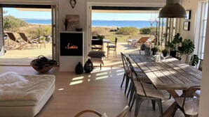 A spacious living area with a wooden ceiling, a mounted TV, and a large window overlooking the beach. - Stunning Ocean View and Private Beach (Nykobing Sjaelland)