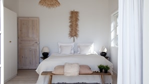 A bedroom with a bed, bedside lamps, a hanging rattan light fixture, a wooden door, and a window with curtains. - Stunning Ocean View and Private Beach (Nykobing Sjaelland)