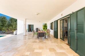 Enjoy dining al fresco under a covered patio with a pool in the background.