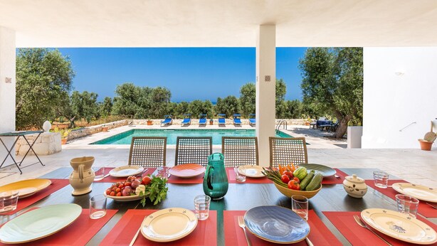 An outdoor dining area with a pool view, red table mats, and a variety of table settings. - 2968 Villa Freude by Perle di Puglia (Carovigno)