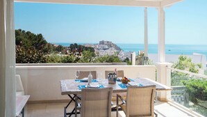 Un balcón con una mesa dispuesta para dos personas, con vistas a un pueblo costero y al mar.