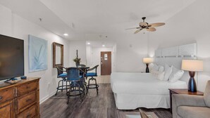 A hotel room with a bed, a desk with chairs, a television, and a ceiling fan. - Studio @ Luau! Walk to beach! Sleeps 4~ (Miramar Beach)