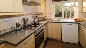 Une cuisine avec des meubles en bois, une cuisinière à gaz, un lave-vaisselle et une fenêtre donnant sur un espace verdoyant.