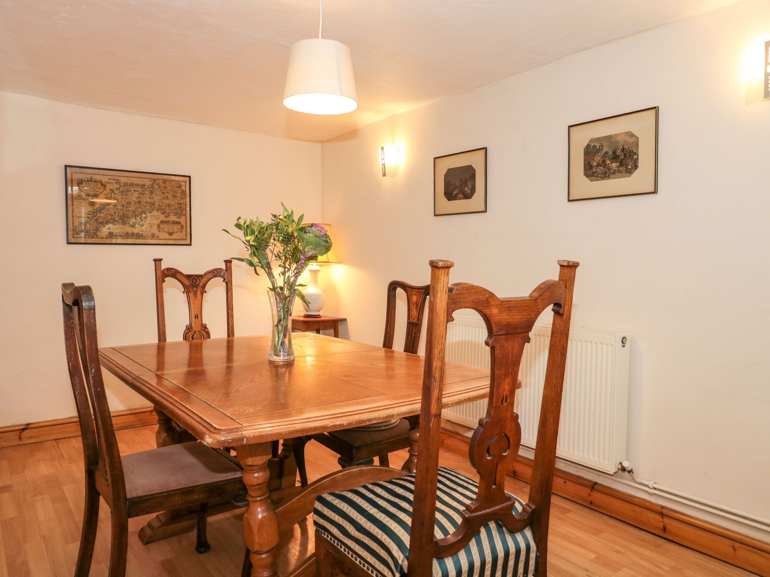 A dining room with a wooden table, six chairs, a vase with flowers, and wall-mounted pictures.