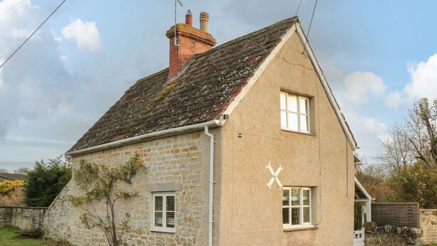 Une maison en pierre avec un toit en pente, une cheminée et une petite fenêtre.