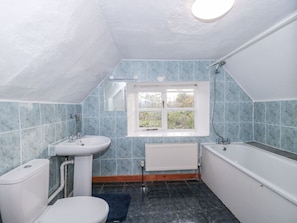 A small, narrow bathroom with a toilet, sink, and bathtub. There is a window providing natural light and a view of greenery outside.