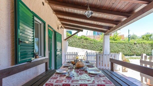 An outdoor dining area with a table set for four, covered by a patterned tablecloth, wooden benches, and a white fence in the background. - 2918 Il Bacio del Sole - Trilocale Matteo by Barbarhouse (Vieste)