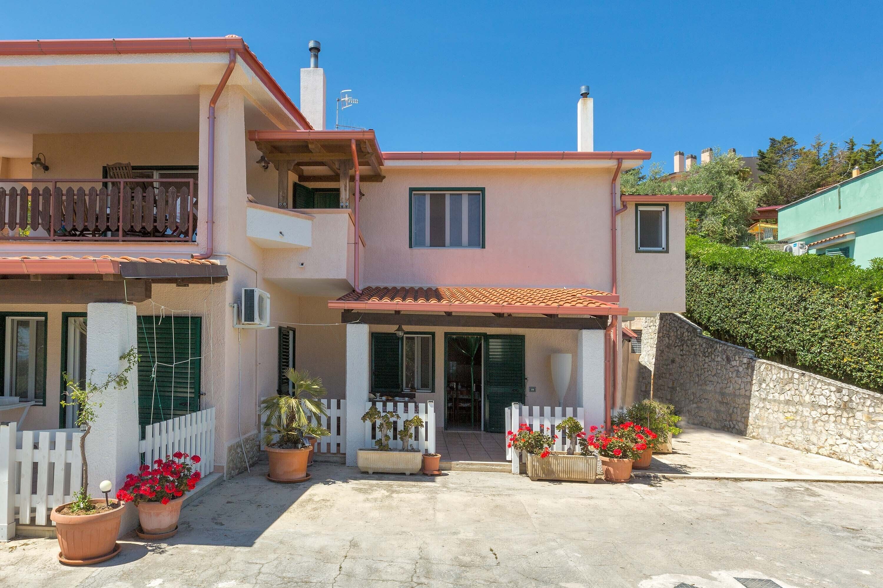 A two-story house with a balcony, a stone wall, and potted plants.