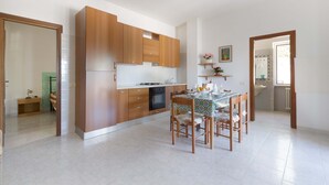 A modern kitchen with wooden cabinets, a dining table with chairs, and a small kitchen island. - 2918 Il Bacio del Sole - Trilocale Matteo by Barbarhouse (Vieste)