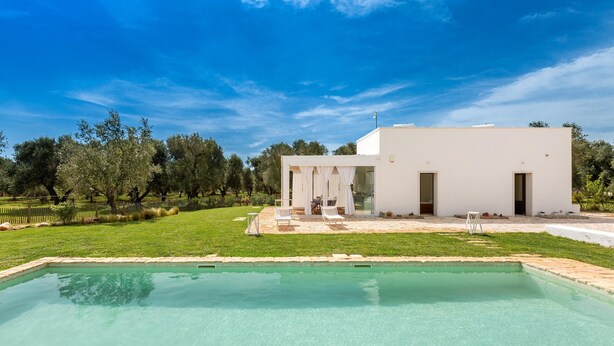 A modern white building with a pool, surrounded by a well-maintained lawn and trees. - 2329 Villa Kairos by Perle di Puglia (Ostuni)