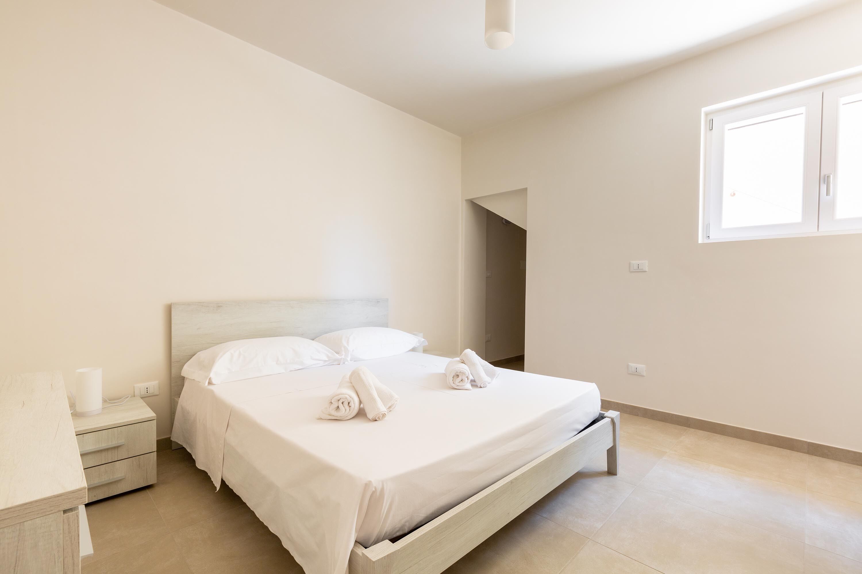 Een minimalistisch ingerichte slaapkamer met een enkel bed, een nachtkastje en een raam.