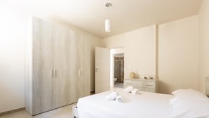 A modern bedroom with a large bed, a wardrobe, and a bathroom visible through an open door. - 2921 Villa La Seta by Perle di Puglia (San Vito dei Normanni)