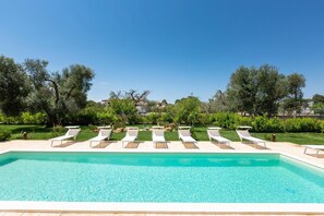 Une piscine avec des chaises longues et un ciel bleu azur.