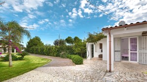 A paved courtyard with a stone floor, surrounded by greenery and a white building with large windows and a door. - 2535 Appartamento Red - Villa Sogno Blu by Barbarhouse (San Vito dei Normanni)