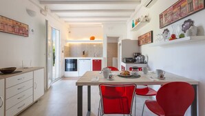 A modern kitchen with a dining area, featuring a wooden table, red chairs, and a variety of kitchen appliances. - 2535 Appartamento Red - Villa Sogno Blu by Barbarhouse (San Vito dei Normanni)